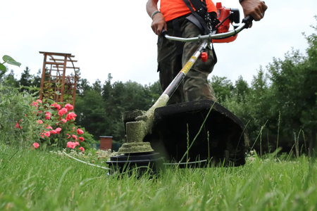 The gardener mows the grass in the garden with a brushcutter