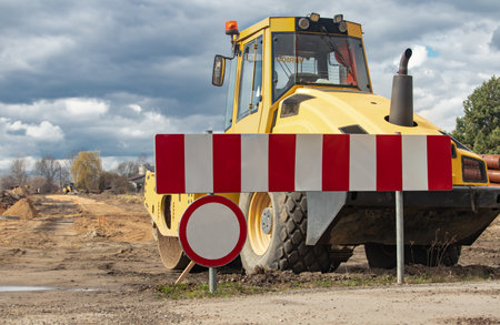 Road construction site with a yellow excavator and red and white warning tapesの写真素材