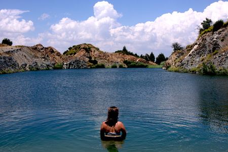 Young, beautiful woman model standing in a lake of a old sandmining place on holiday in Spain. With a cloudy skyの写真素材