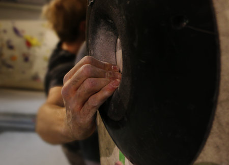 A person or man climbing up a wall and holding a black grip with dirty hands full of magnesium for fun during a bouldering sessionの写真素材