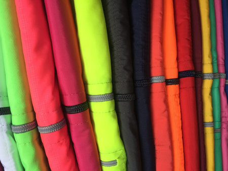 A high pile of jackets with many bright, fluoriscent colors and a zipper in the middle