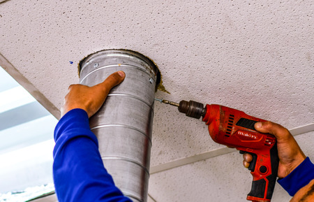 Technician screw with a power drill to install vents galvanized circular hole in the ceiling. With the intention, skill, care is better.の写真素材