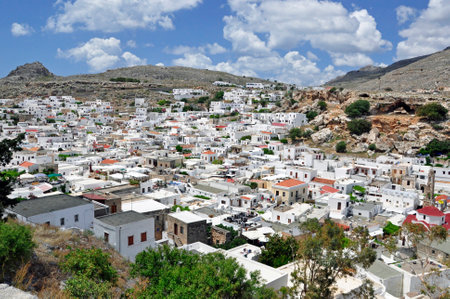 A view from above of the white town of Lindos in Rhodes, on a sunny day, with the sky covered with white clouds. Greece.の写真素材