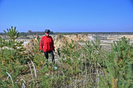 A cyclist in a helmet and a red jacket stopped at the marl excavation, among grass and small trees.の写真素材