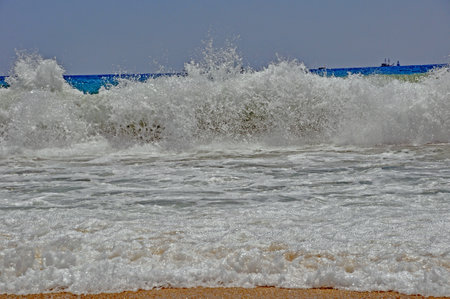 A sea wave approaching the shore, agitated water, in the background a gray -blue sky and a ship on the horizon.の写真素材
