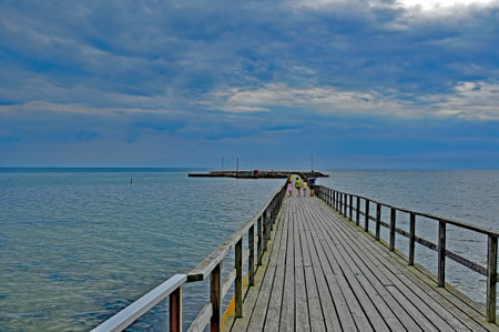 On a cloudy afternoon, a family with children goes a gangway from the beach to a small fishing marina in Arnager, Bornholm, Denmark.の写真素材