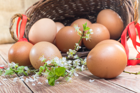 Easter - Detail on Spilled Hen Eggs in a Wicker Basket with a Ribbon and Spring Flowers on Wooden Tableの写真素材