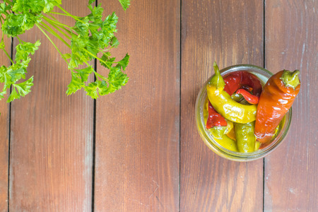 Top View on Open Pickled Chilli Peppers in Glass Jar with Parsley on Wooden Tableの写真素材