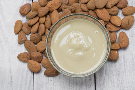 Top View on a Almond Butter in a Glass Bowl with Almonds on Wooden Backgroundの写真素材