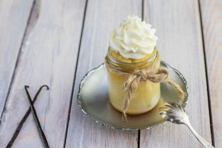 Baked pudding made from egg yolks in jar with whipped cream and vanilla pod on small tin plateの写真素材