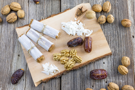 Three Dates bar wrapped in paper with walnuts and coconut on a wooden board top viewの写真素材