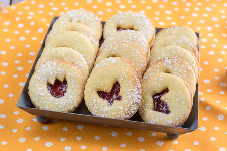 Detailed Linzer Easter cookies with a strawberry jam, dusted with sugar arranged on tin tray on orange clothtableの写真素材