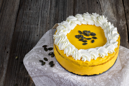 Pumpkin cake with caramel cream and whipped cream with pumpkin seeds on wooden tableの写真素材