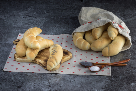 Homemade Traditional Czech pastry - white bread roll (rohlik) with salt and poppy seeds on a wooden board and in a linen bag on a marble backgroundの写真素材