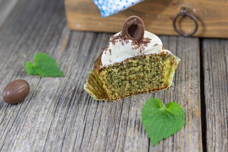 slice of nettle cupcake with mascarpone and white chocolate cream and chocolate easter egg set on old wood tableの写真素材