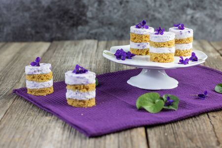 violet flower small cakes with mascarpone violaceous cream set on old wood tableの写真素材
