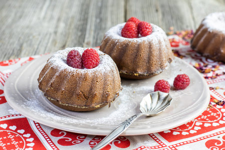Sugared raspberry chocolate mini cakes on brown plateの写真素材