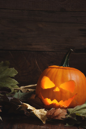 Halloween Pumpkin with glowing eyes and teeth on the leaves with a wooden backgroundの写真素材