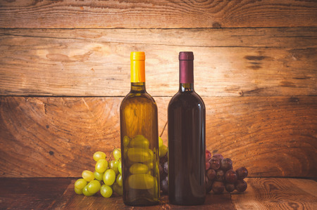 Red and white wine bottle with grapes and barrel on wooden rustic table.の写真素材