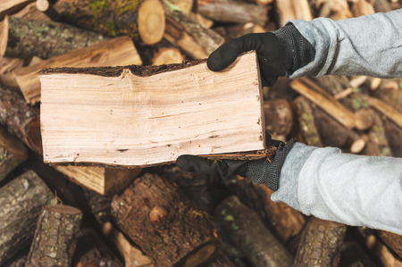 Firewood in a piece of wood stored on the stack, hands holding a piece of firewoodの写真素材