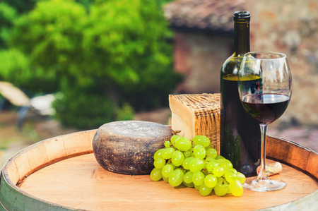 Red wine, pecorino cheese on a wooden barrel in the background of the Tuscan landscape, Italyの写真素材