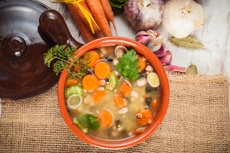 Rural vegetarian broth soup with colorful vegetables and rustic clay pot.の写真素材