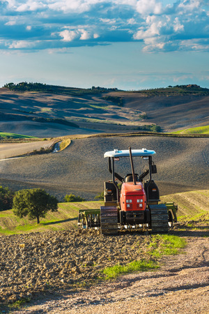 Red tractor on tracks in the landscape of Tuscany and cloudy skiesの写真素材