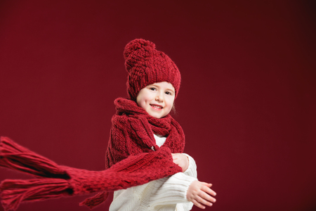Beautiful blond girl playing in the winter warm hat and scarf on red backgroundの写真素材