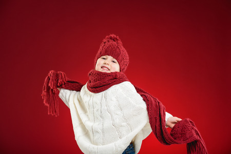 Beautiful blond girl playing in the winter warm hat and scarf on red backgroundの写真素材
