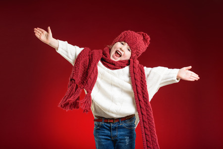 Beautiful blond girl playing in the winter warm hat and scarf on red backgroundの写真素材
