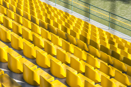 Back view through wired fence yellow stadium stands seats, sunny dayの写真素材
