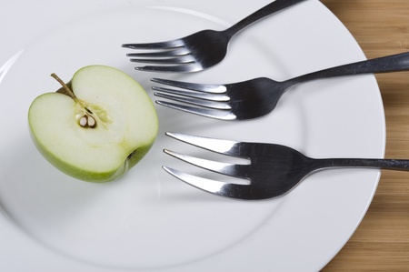 Green apple on the white plate with forkの写真素材