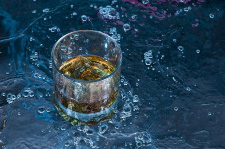 Glass of whisky on a background splashing dark water