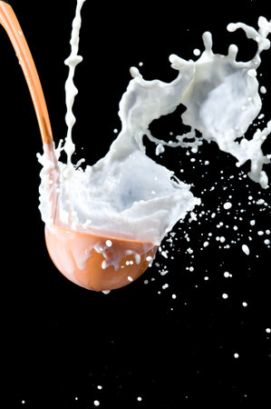 Scoop and splashing milk on black background. Pouring milkの写真素材