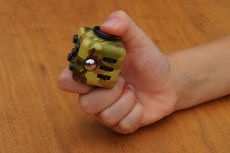 Child hand holding a fidget cube against a wooden backgroundの写真素材