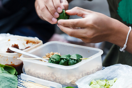 Food wrapped in leaves or Miang Kham with hand of seller background at local market, Thailandの写真素材