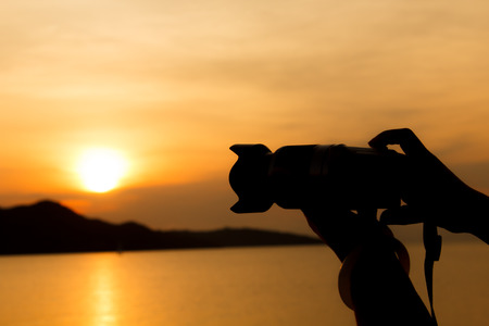 silhouette of woman hand using the digital camera take phothos when sunriseの写真素材