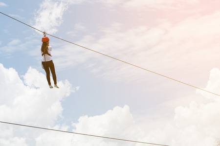 side view of young woman riding on zip line against skyの写真素材