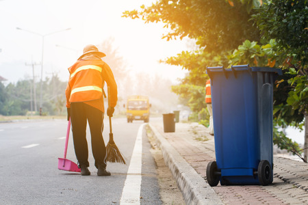 Blue trash bin with worker cleaning the road background on daytimeの写真素材