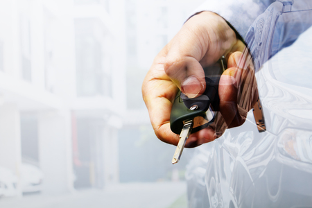 Double exposure with car key in hand and car parking in line near the building backgroundの写真素材