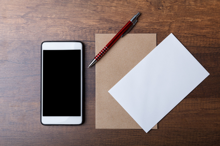 Flat lay of brown envelope with pen and smartphone on wooden background. It represents the symbol of human communication before being replaced by a smartphone.の写真素材