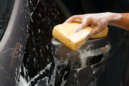Closeup photo of employee hand washing car with yellow sponge in car wash shop.の写真素材
