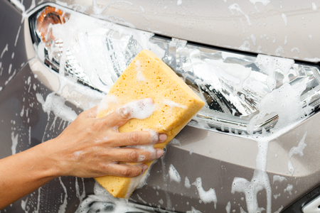 Closeup photo of employee hand washing car mirror with yellow sponge in car wash shop.の写真素材