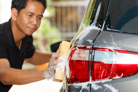 The rear view photo of the car washing in the car wash shop with a blur image of the cleaning staff in the back.の写真素材
