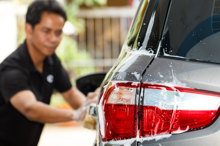 The rear view photo of the car washing in the car wash shop with a blur image of the cleaning staff in the back.の写真素材