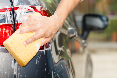 The rear view photo of employee hand washing car with yellow sponge in car wash shopの写真素材