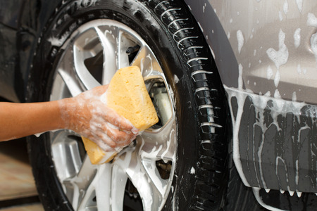 employee hand washing car wheel with yellow sponge in car wash shop, selective focusの写真素材