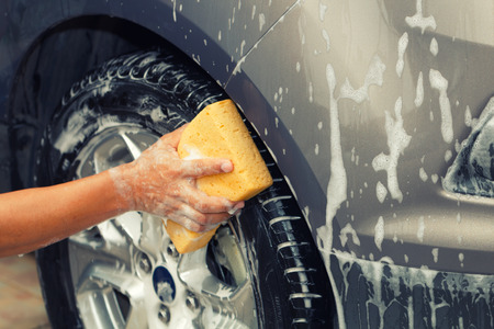 Closeup photo of employee hand washing car wheel with yellow sponge in car wash shop.の写真素材