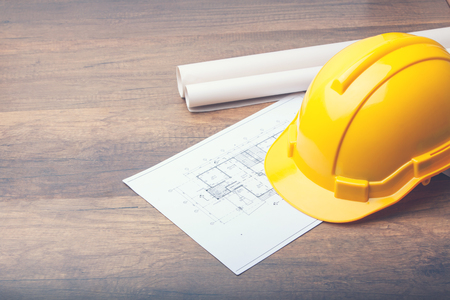 The yellow Hard hat construction plans on wooden board. Shows the concept of architects and builders who are designing and building houses.の写真素材