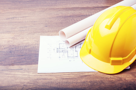 The yellow hard hat construction plans on wooden board. Shows the concept of architects and builders who are designing and building houses.の写真素材